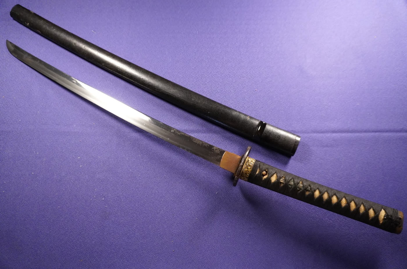 Kunikane wakizashi drawn beside its black-lacquered saya on purple cloth