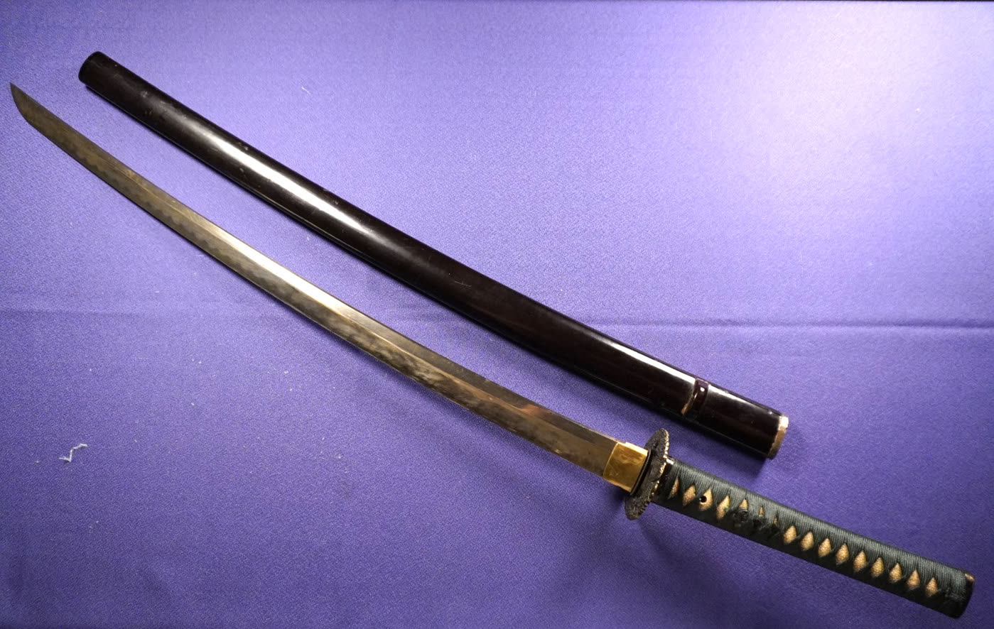 Katana drawn beside its black-lacquered saya and mounted tsuka on purple cloth