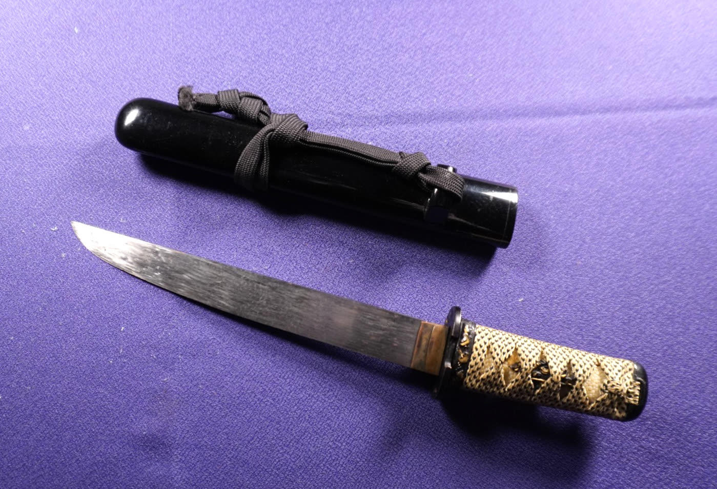 Tantō drawn beside its black-lacquered saya with the cord tied around it